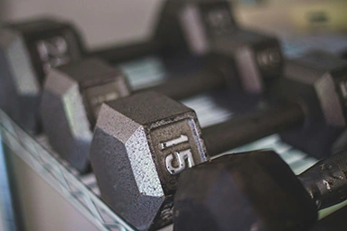A set of 4 black dumbell weights on a rack in a gym with the number 15 on one of them.