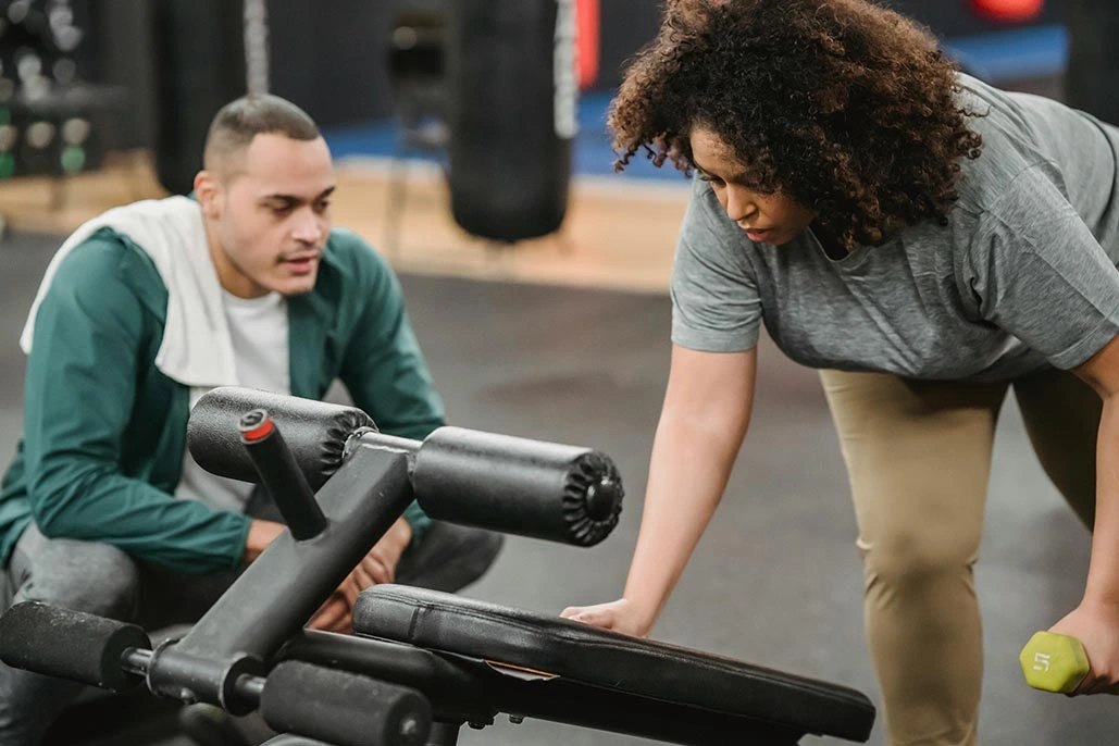 Personal trainer working with client and helping her with her form using light weight.